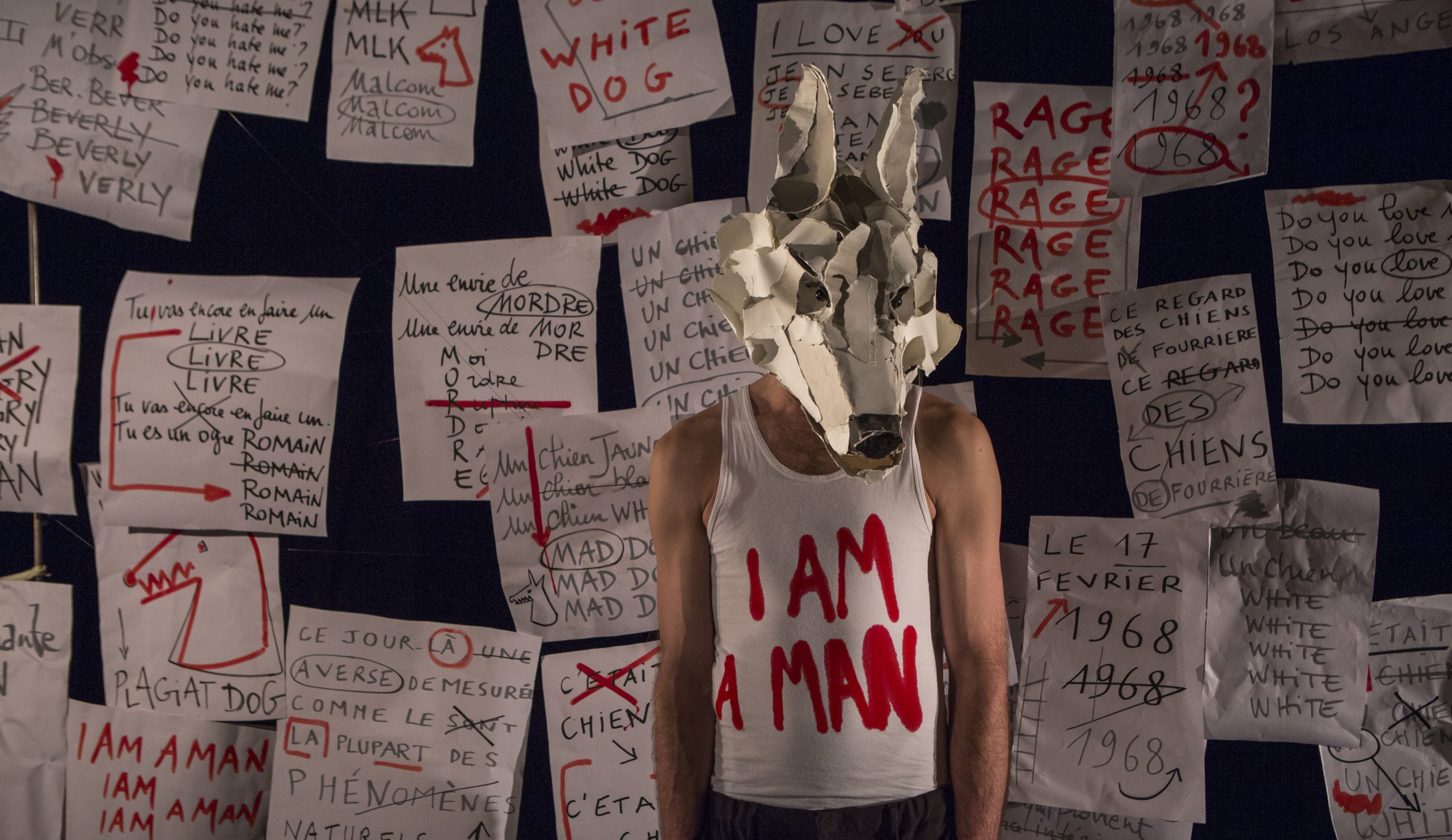 mann med hundemaske foran en rekke papiroppslag